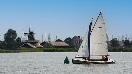 Zeilboot op meer met molen op achtergrond.